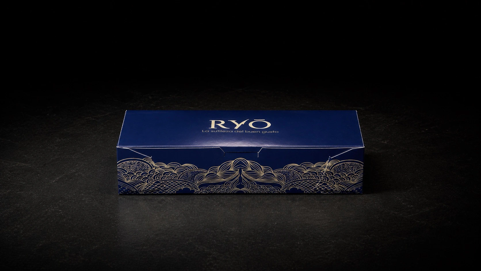 Caja azul RYŌ cerrada y centrada en una escena de estudio oscura